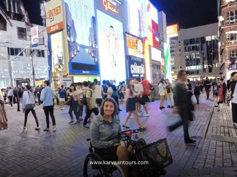 Traveler in a wheelchair at Dotonbori street in Osaka at night with bright neon signs and crowds around