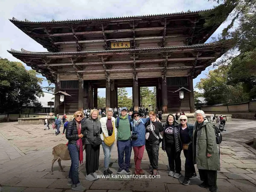 A group of senior travelers walking towards the massive, historic wooden Nandaimon Gate at Todai-ji Temple in Nara, Japan, surrounded by the park's lush greenery.