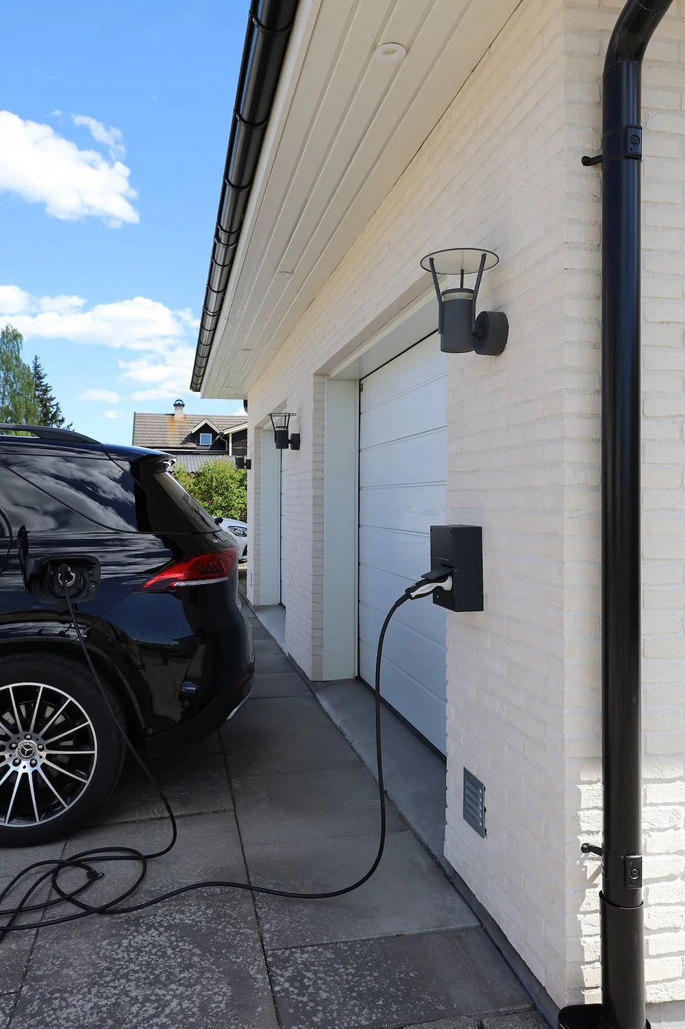 Ladeboks monteret ved garage på hvidt murstenshus med ladekabel til bilen