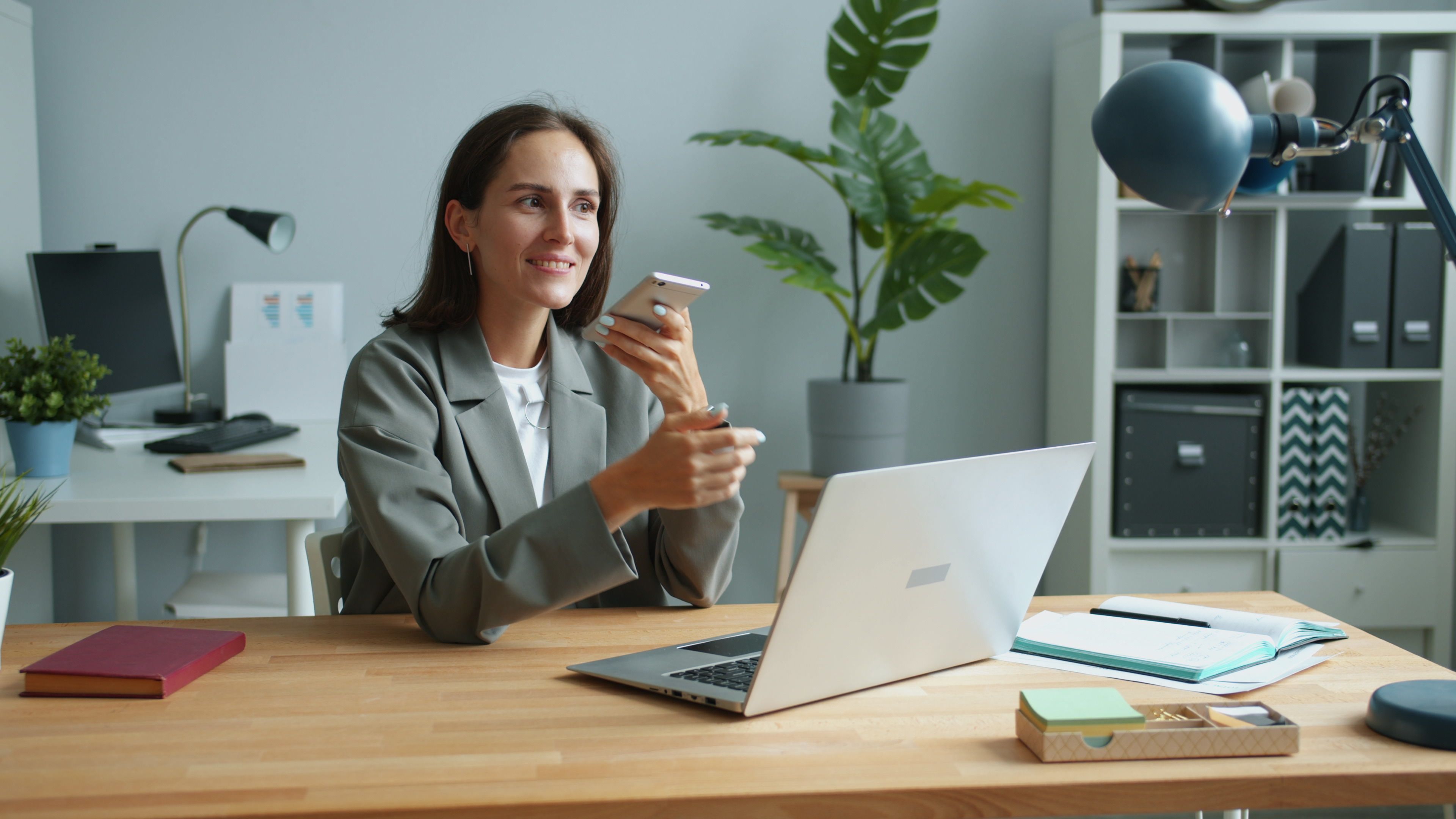Employee using a personal smartphone alongside a work laptop in an office, highlighting BYOD security risks and personal device use in the workplace.