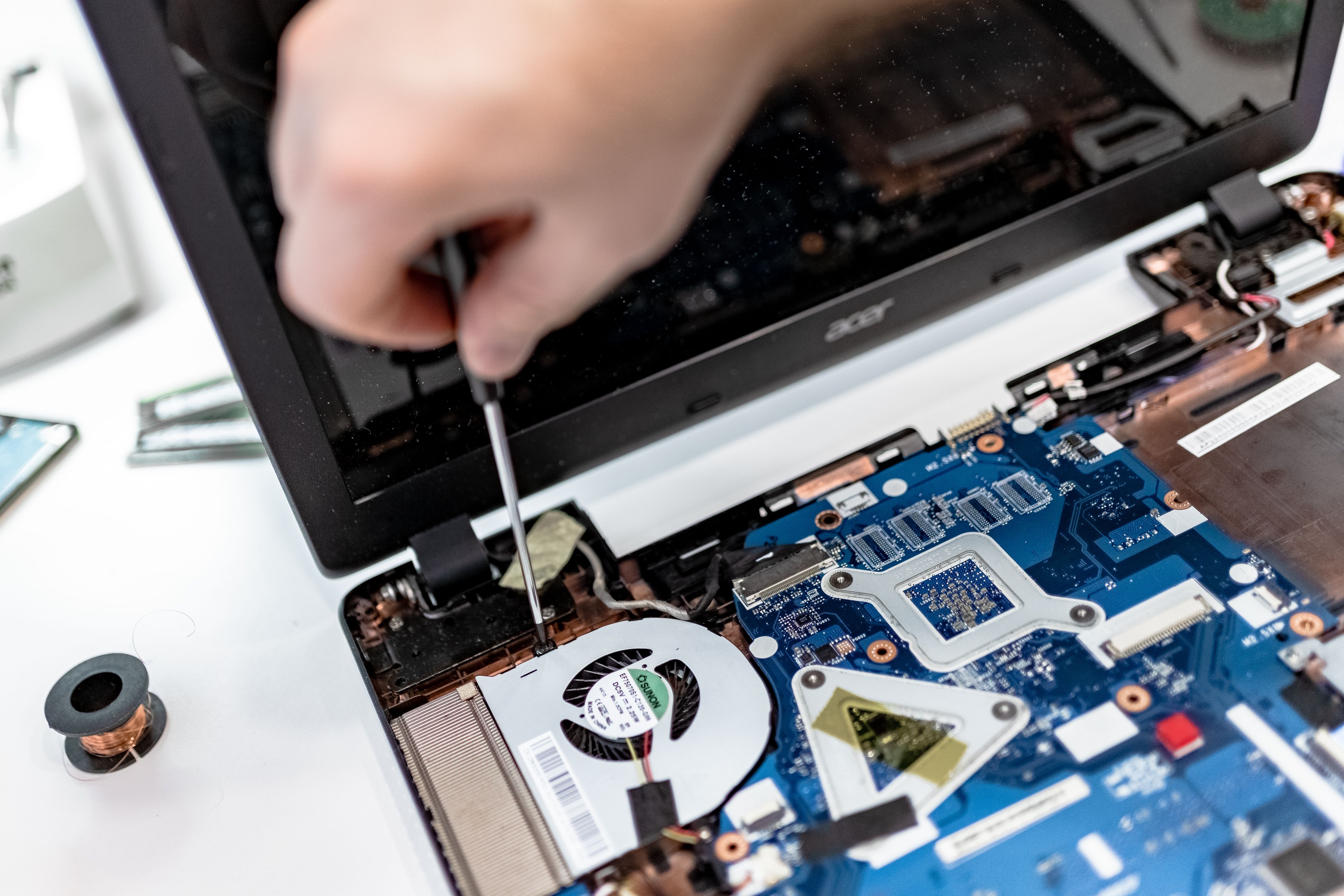 Technician using a screwdriver to repair internal laptop components, including the cooling fan and motherboard.