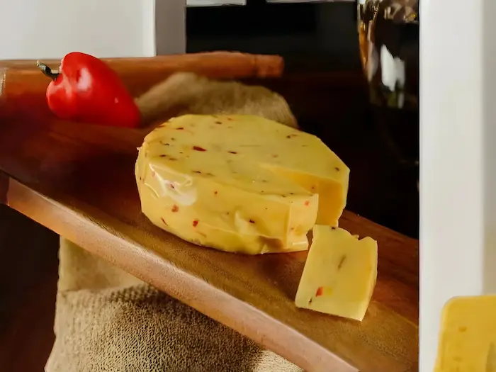 Queso Maduro con peuqeñas cantidades de chile dentro del queso, encima de una mesa de madera con un fondo oscuro de madera y un chile alrededor