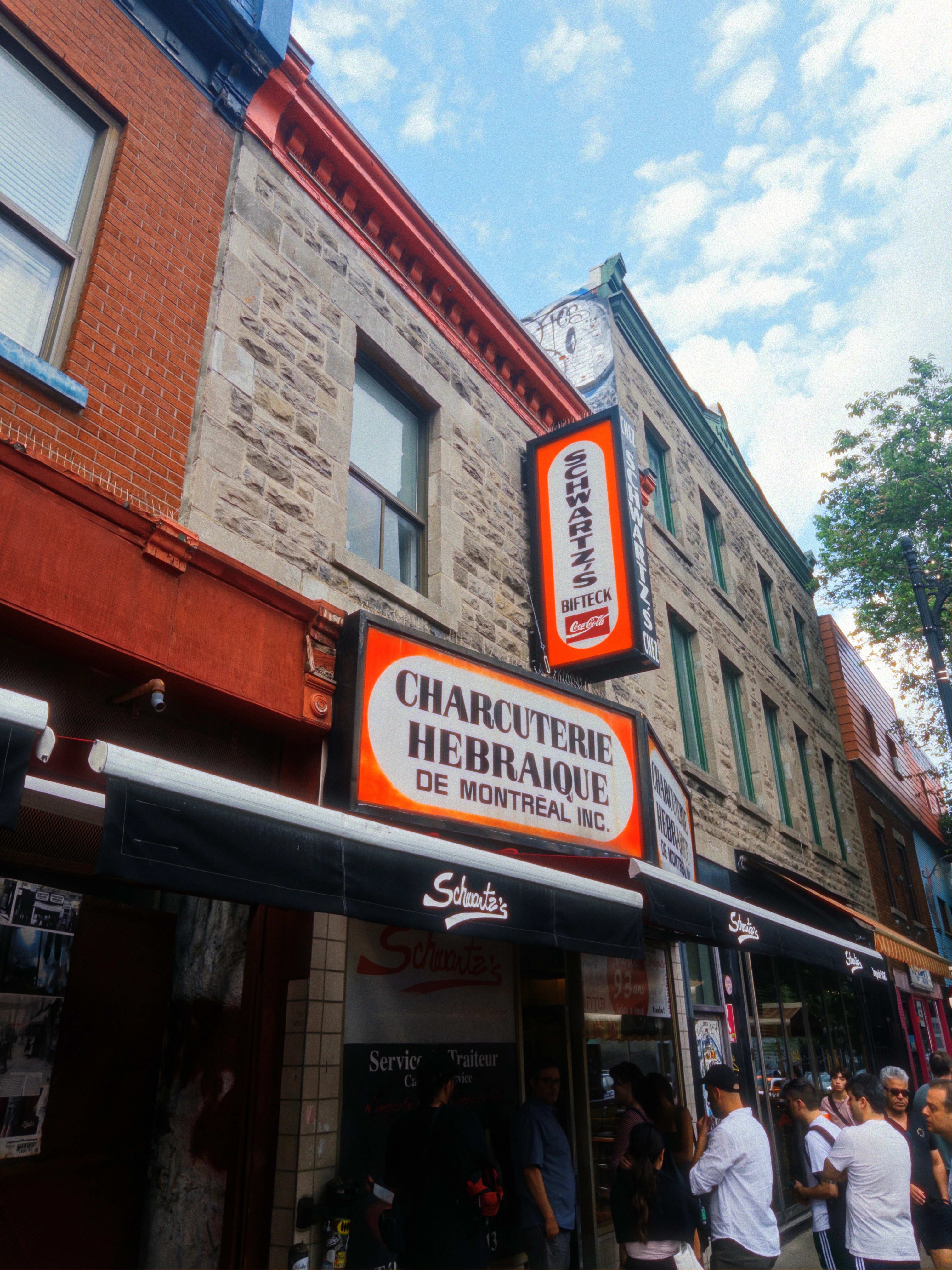 The exterior of the world-famous Schwartz' Deli, with a line on the sidewalk to get in.