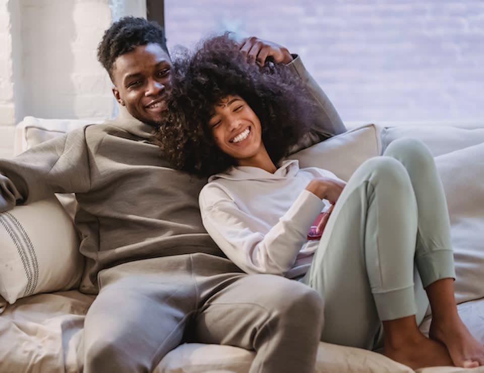 Man and woman in loungewear on a couch smiling and cuddling