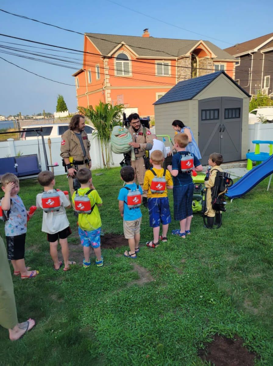 NYC Ghostbusters demonstrate how to catch a ghost with a puppet slimer to a group of children for a birthday party.