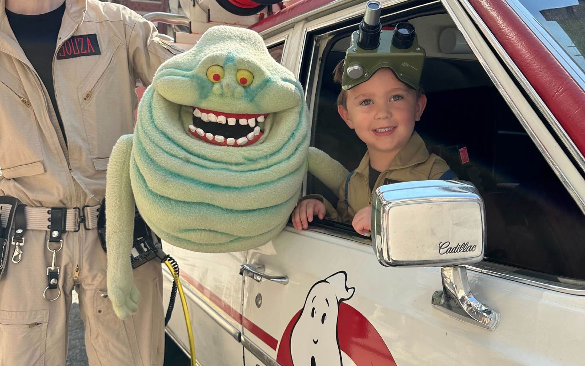 A birthday boy celebrating his birthday with the NYC Ghostbusters inside of an Ecto-1 replica with a Slimer puppet.