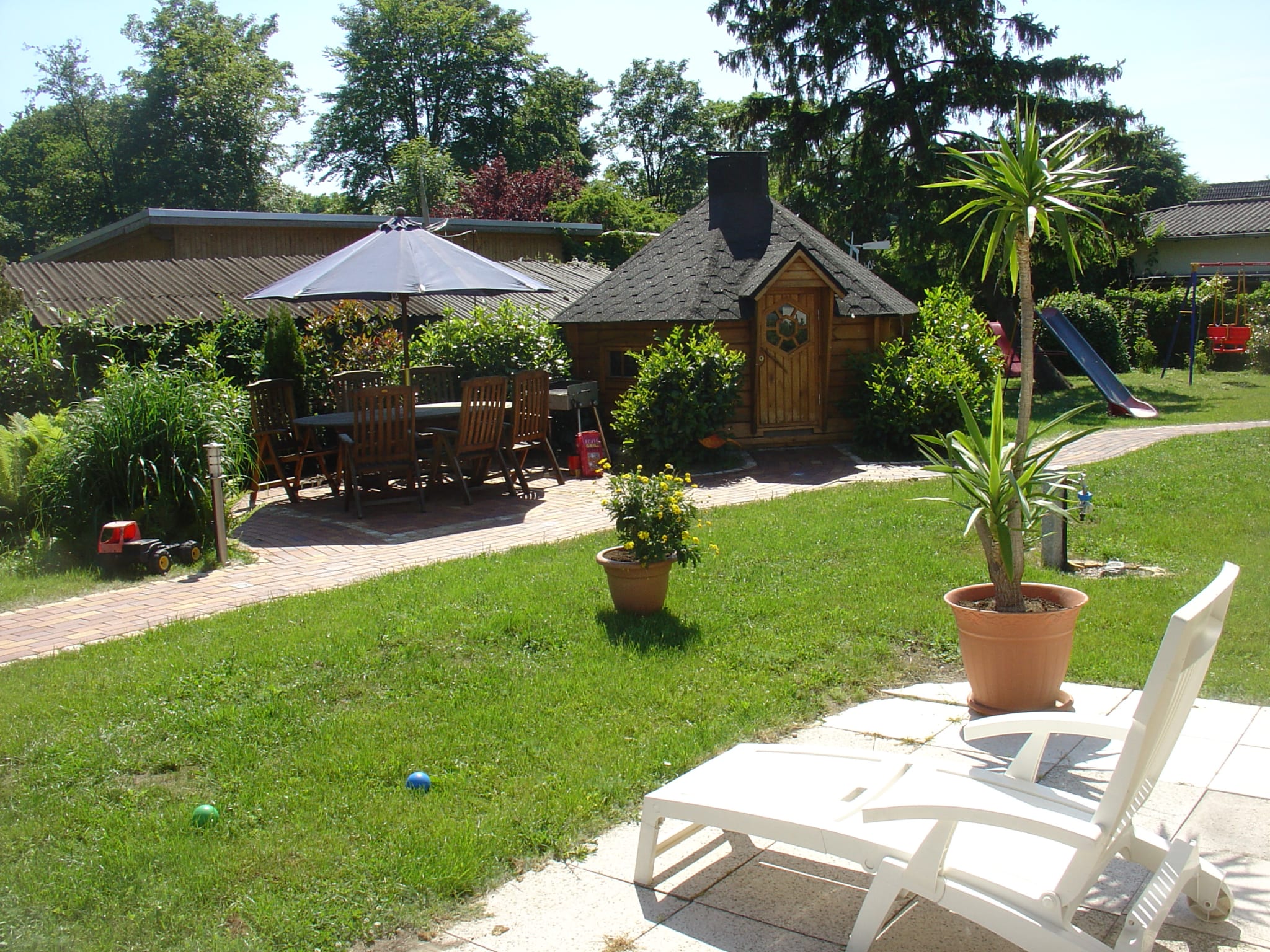 Finnische Grillkota und ein Esstisch mit 6 Stühlen unter einem Sonnenschirm