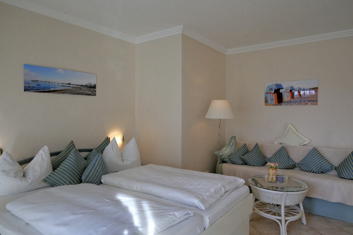 Doppelbett mit Sofa im Hintergrund. 2 Bilder an der Wand.