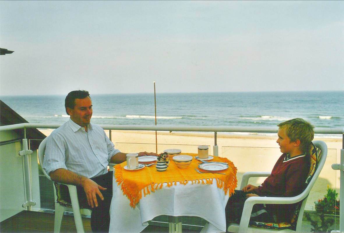 Ein Mann und ein Kind auf einem Balkon mit dem Strand und der Ostsee im Hintergrund