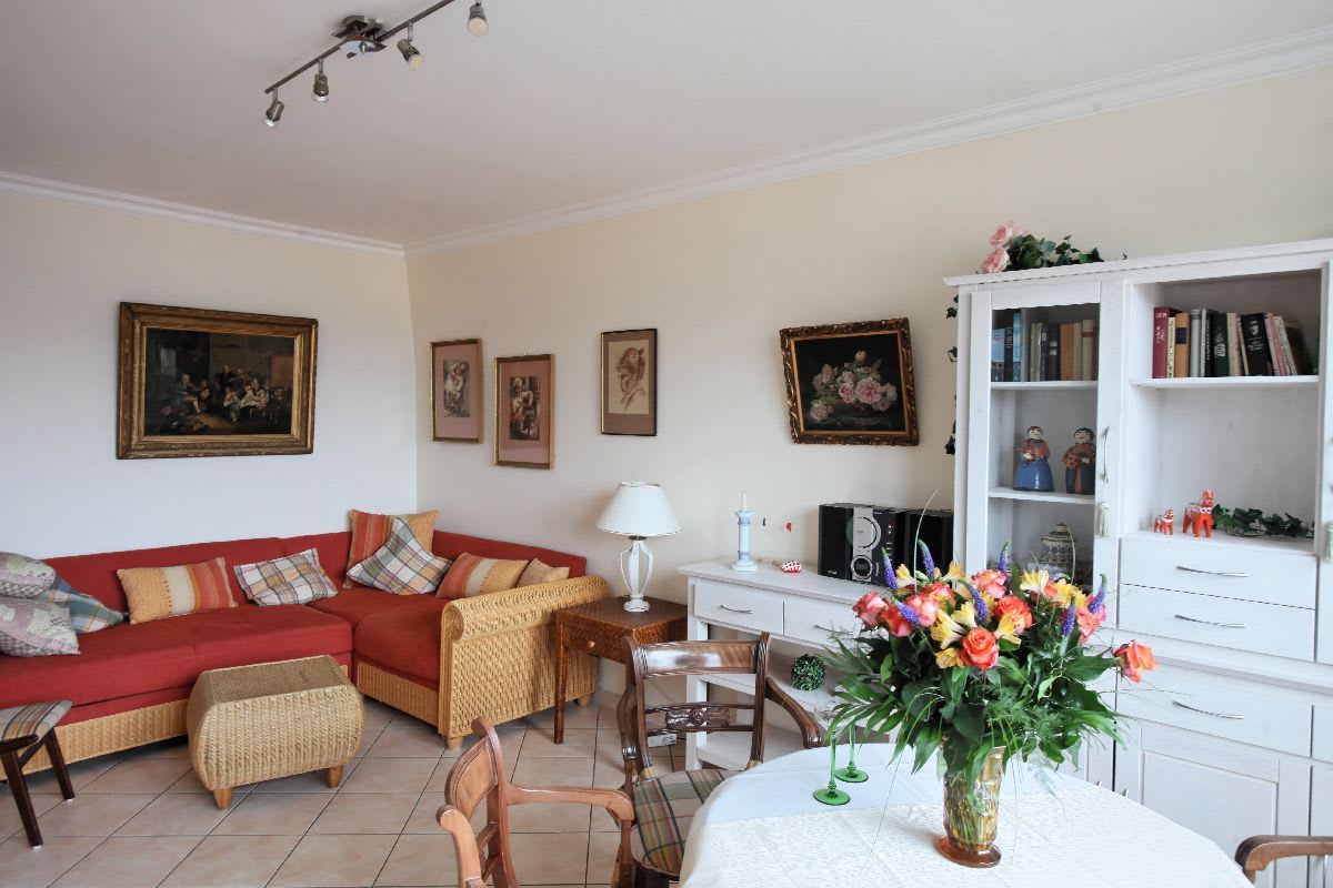 Wohnzimmer mit Esstisch und Couch, an der Wand hängen viele Gemälde