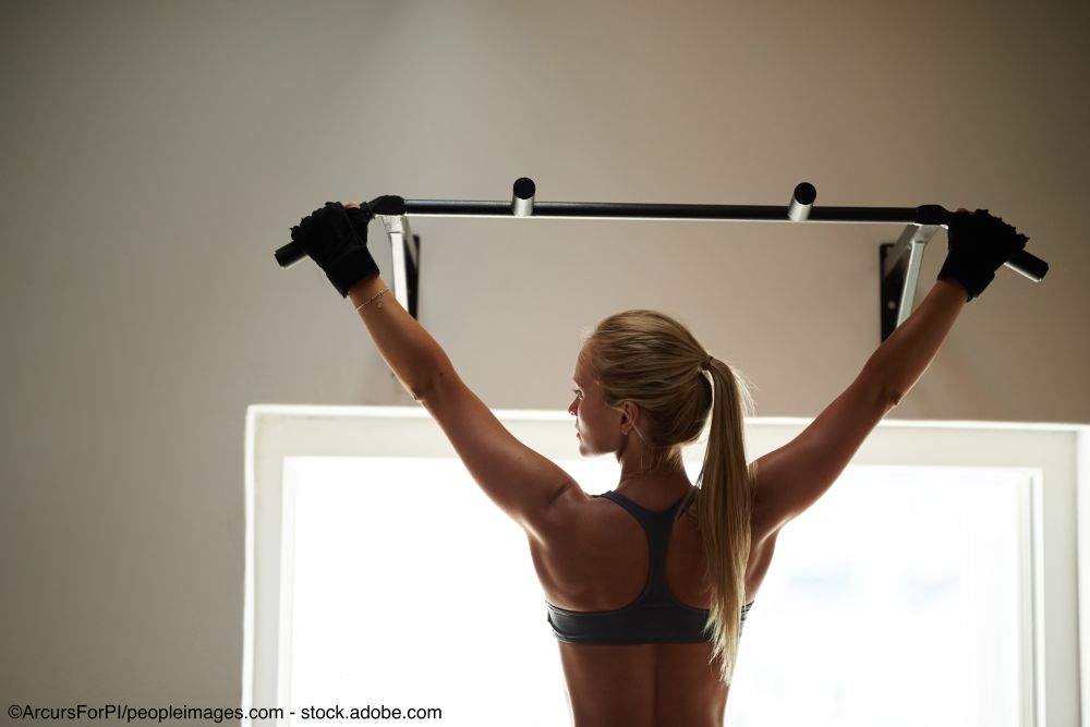 Frau macht Klimmzüge and einer Klimmzugstange zu Hause