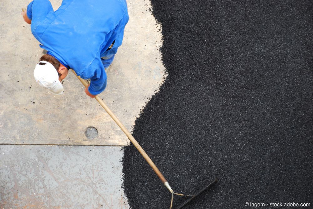 Arbeiter verteilt frischen Asphalt mit einer Harke auf einer Einfahrt