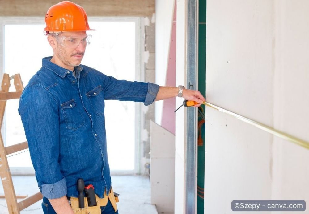 Handwerker misst mit dem Zollstock skeptisch Wand aus