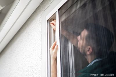 Un artisan sympathique installe des moustiquaires au domicile d'un client