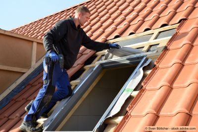 Un couvreur installe des fenêtres de toit "Velux" sur les toits de tuiles rouges dans le bâtiment