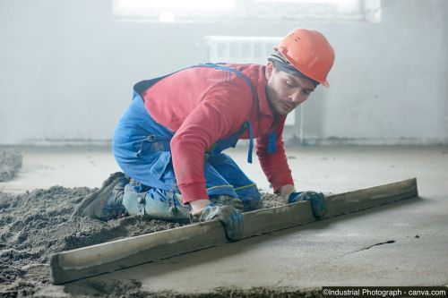 Ouvrier qui lisse une chape ciment sur un chantier intérieur