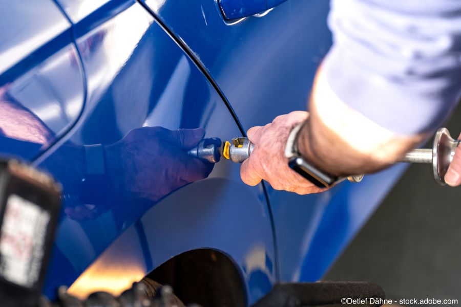 Fachmann versucht einen Hagelschaden am Auto zu beseitigen