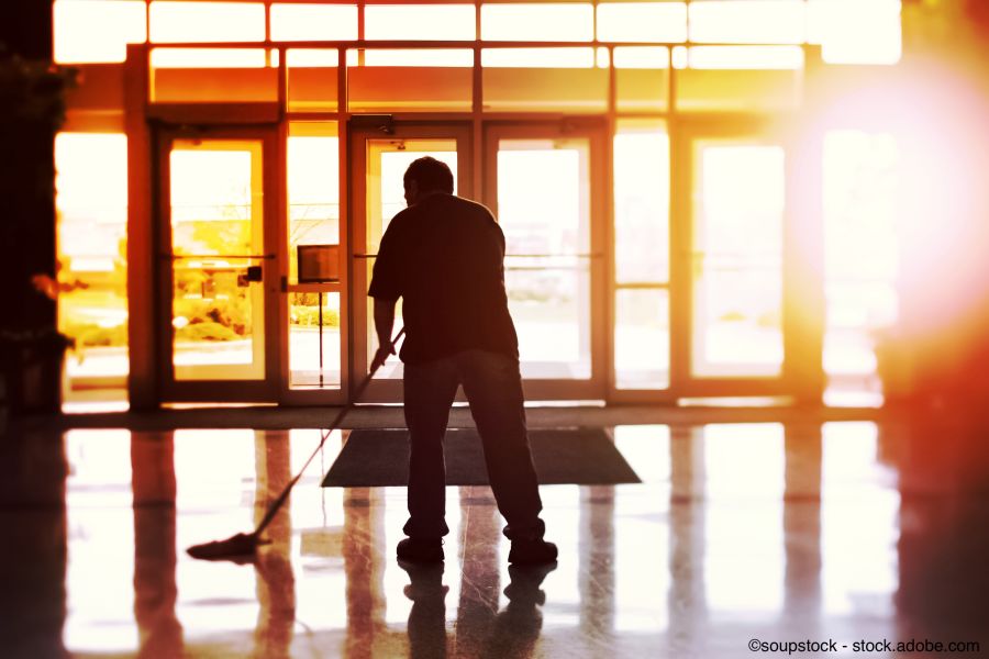 Hauswartungskraft reinigt einen glänzenden Eingangsbereich bei Sonnenuntergang