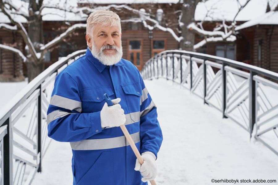 Hauswart in blauer Arbeitskleidung räumt Schnee vor einem Gebäude