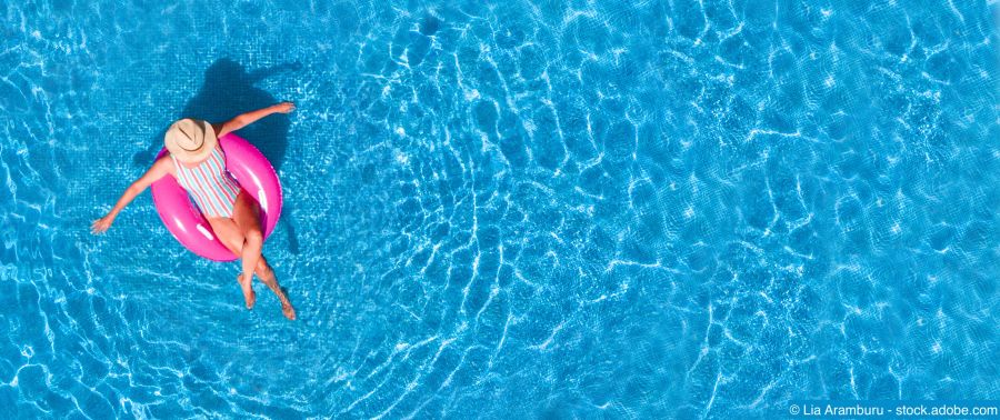 Luftaufnahme eines Schwimmbads: Junges Mädchen in Badeanzug und Hut, das mit einem rosa Donut im Wasser treibt