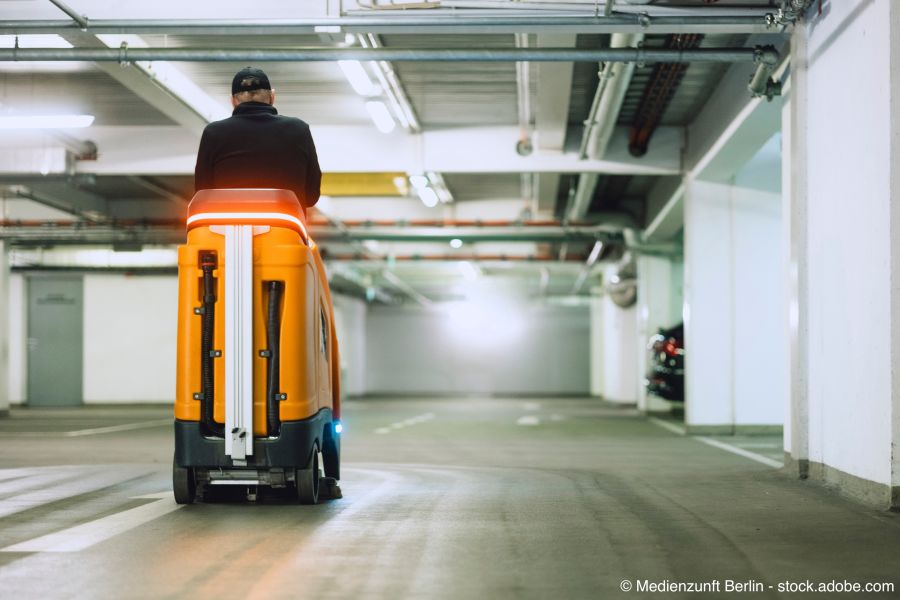 Reinigungskraft wischt den Boden einer Tiefgarage mit Wischmaschine 