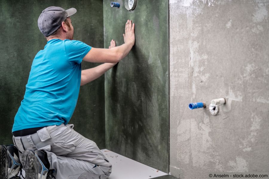 Handwerker montiert XXL Fliese an die Wand in der Dusche