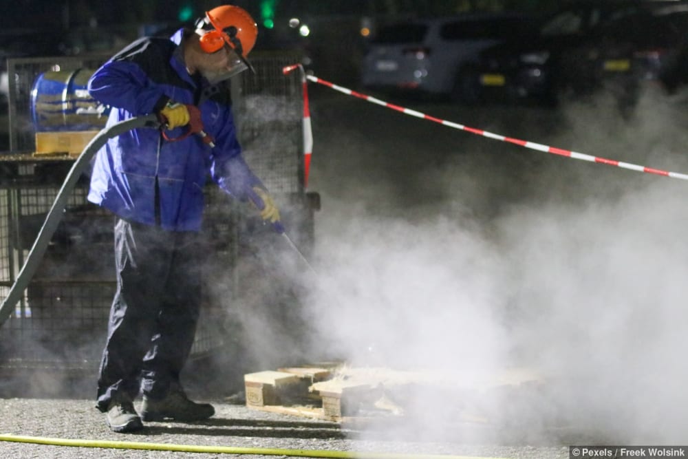 Mann in Schutzkleidung reinigt Aussenbereich einer Baustelle mit Hochdruckreiniger
