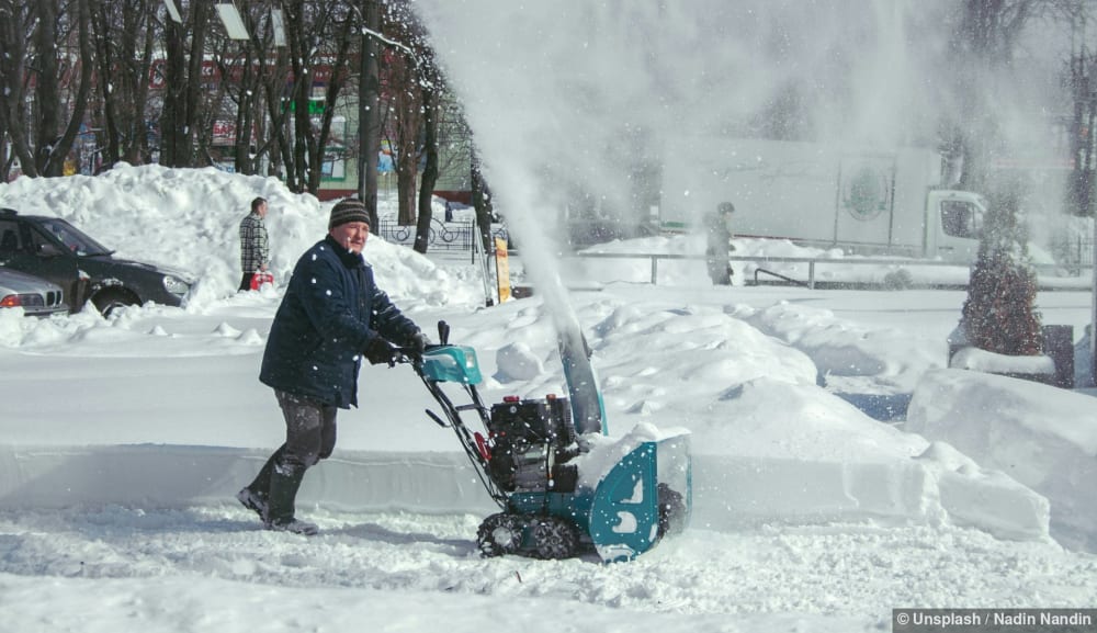 Winterdienst mit der Schneefräse: Ein Mann räumt einen Weg neben einem Parkplatz