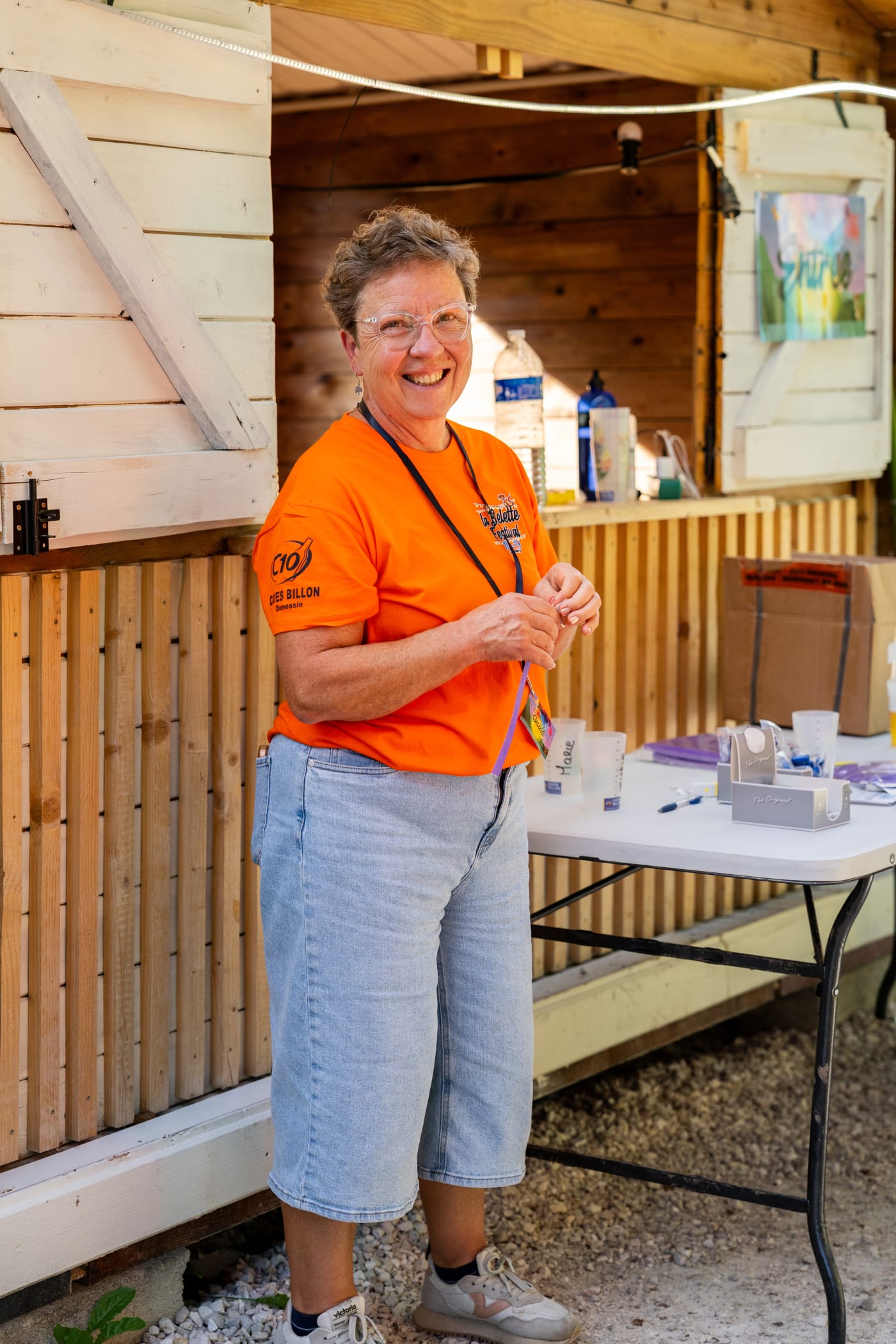Femme en t-shirt orange souriante devant un stand, en journée