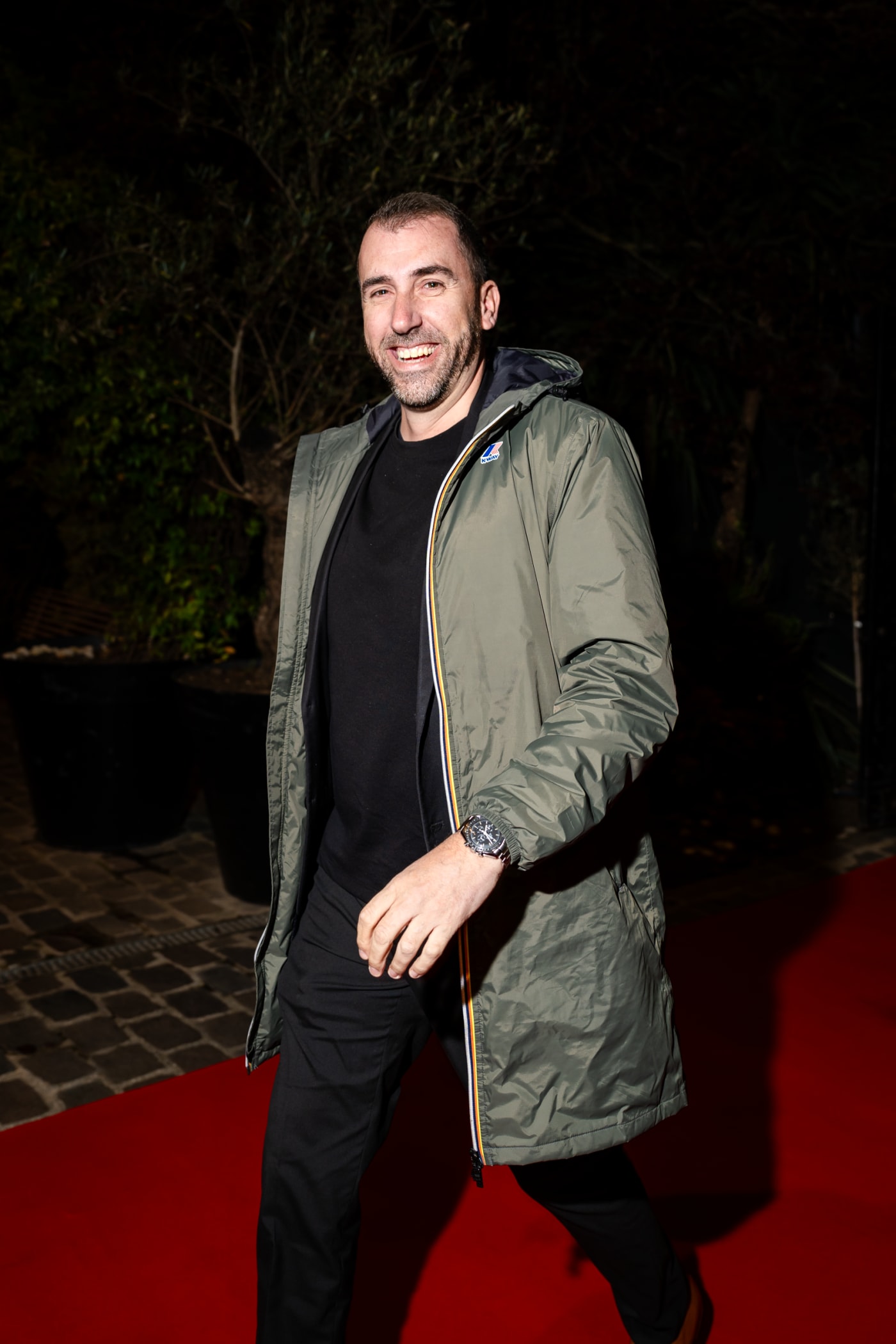 Homme en veste kaki souriant sur un tapis rouge