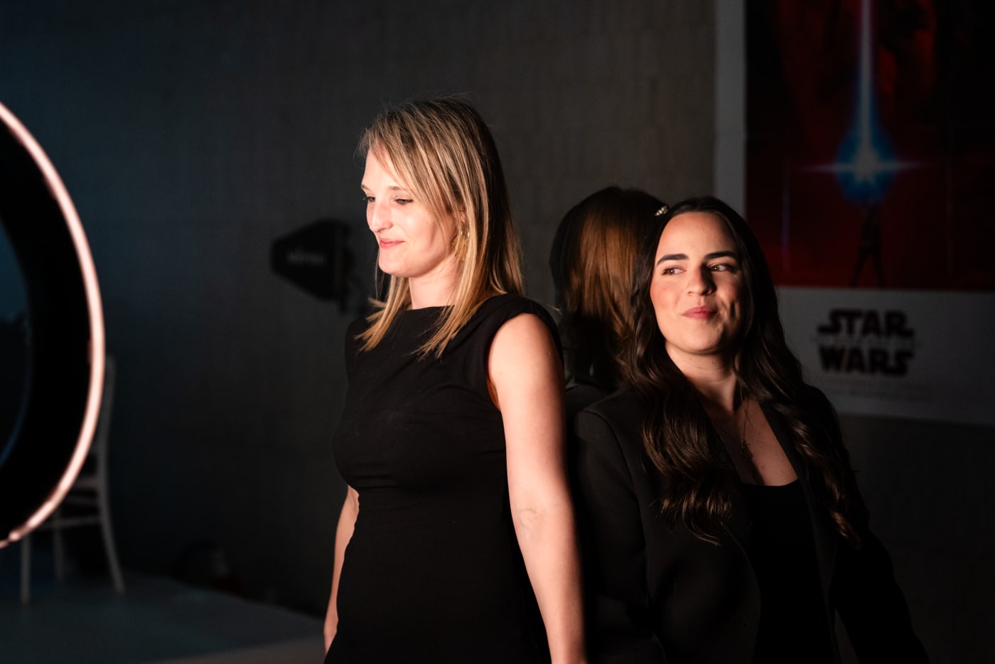 Invitées en robes noires souriant devant un cerceau lumineux