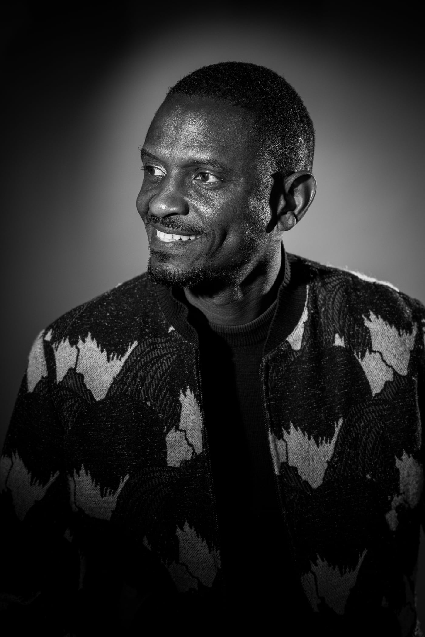 Portrait d’un homme au sourire franc, veste à motifs, fond noir dégradé