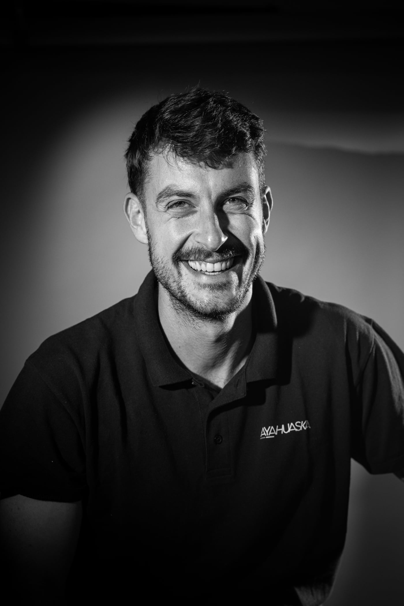 Portrait en noir et blanc d’un homme souriant, en tenue sombre, lors de la soirée Ayahuaska