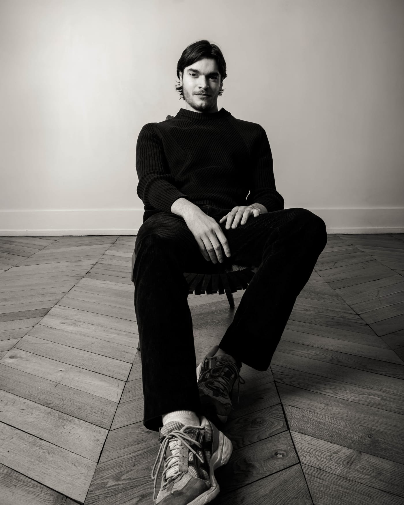 Designer assis sur une chaise, coudes sur les genoux, baskets claires au premier plan