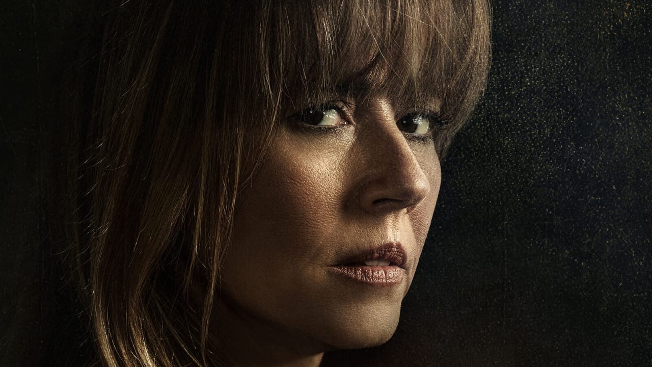 Close de Linda Cardellini como Pamela Voorhees, de franja e cabelos castanhos, olhando de lado com ar desconfiado diante de um fundo escuro