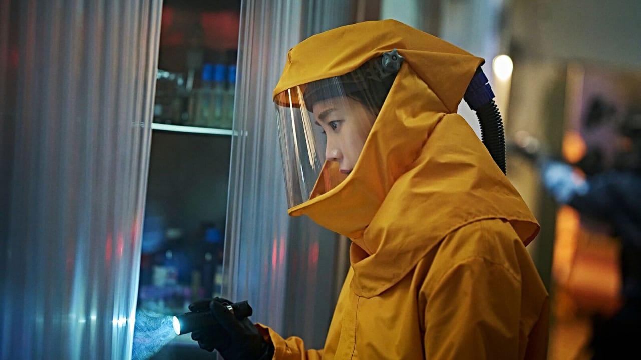 Jun Ji-hyun como a professora Kwon Se-jeong, de traje de proteção amarelo e viseira, examina um armário com uma lanterna