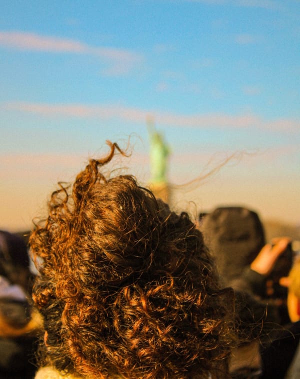 Windblown curly hair lit by the sun, seen from behind in a crowd