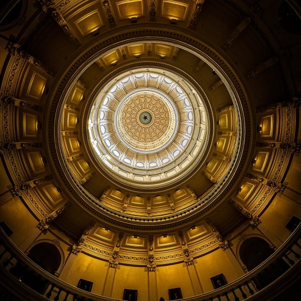 Upward view of an ornate gold-toned domed ceiling and circular skylight