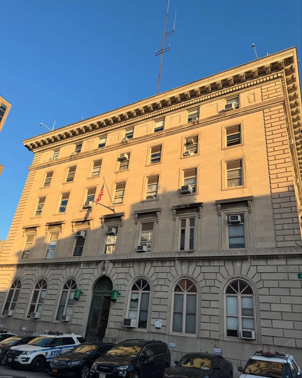 Sunlight and shadow across a stone building with parked cars below