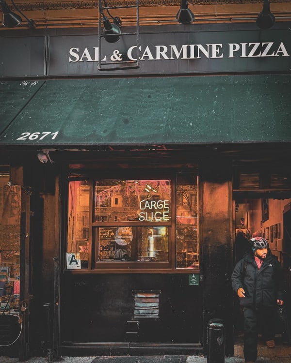 A person standing outside Sal and Carmine Pizza beneath a green awning