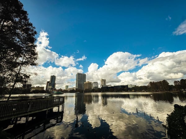City buildings and clouds reflected in a lake beside a wooden boardwalk