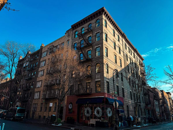 A brick apartment building on a street corner beneath a clear blue sky