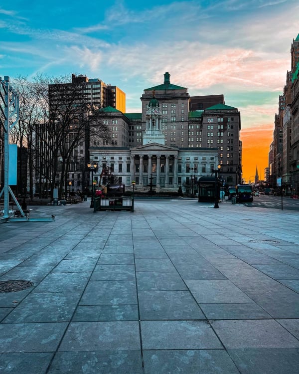 A broad paved plaza leading toward city buildings at sunset