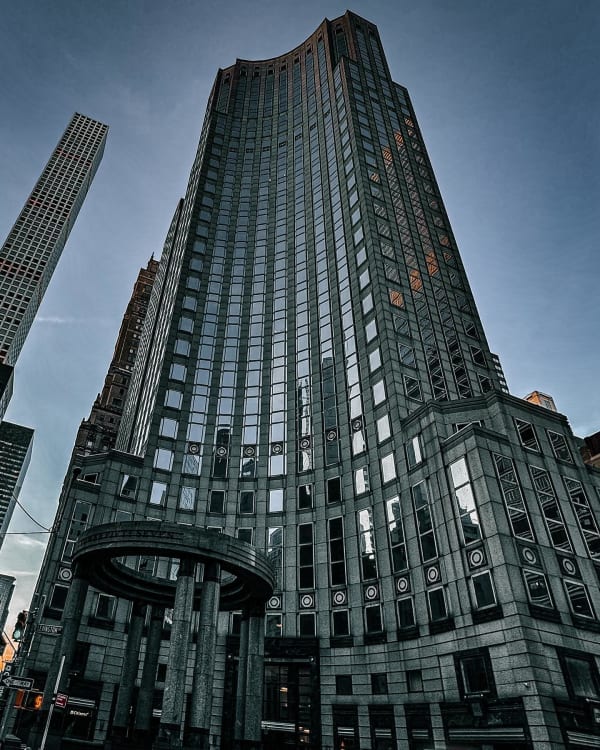 Upward view of a tall glass-and-stone building beneath a gray sky