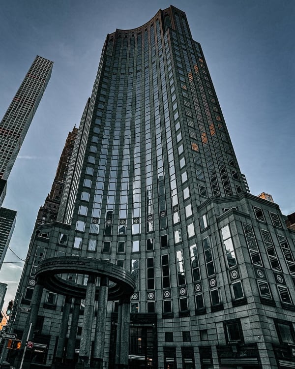 Upward view of a tall glass-and-stone building beneath a gray sky