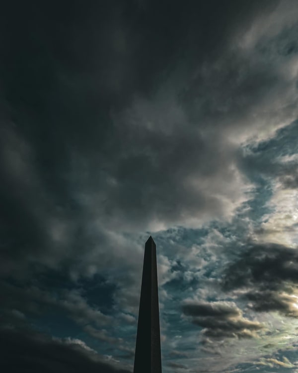 An obelisk rising beneath dark, heavy clouds
