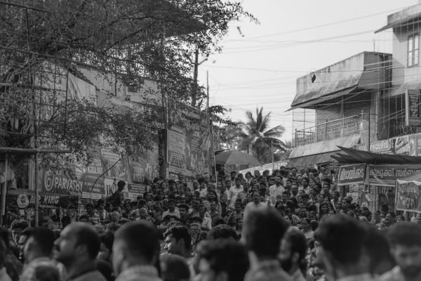 Black-and-white photograph of a crowd filling a street lined with shops