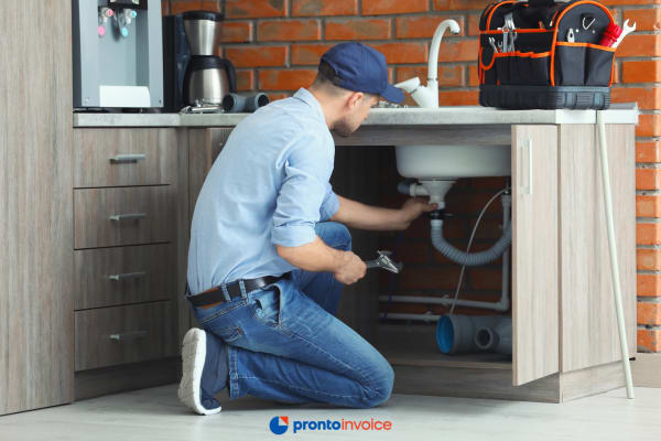 A handyman reviews his smartphone in a finished home entryway with tools nearby, preparing to invoice the client before leaving.