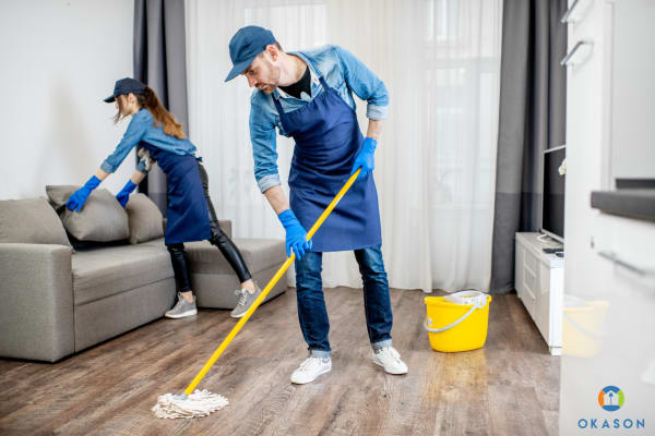 A cleaning business owner in an apron reviews a professional invoice on her smartphone in a freshly cleaned residential kitchen.