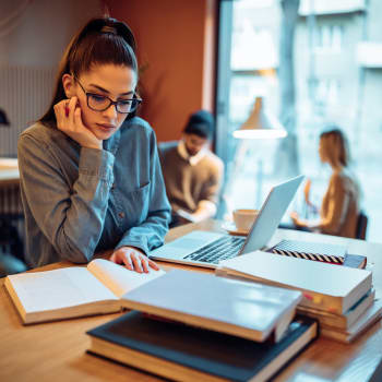 Image of young woman studying behind a desk of books and a laptop
